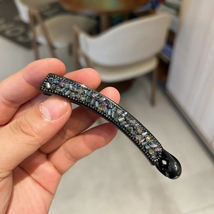 Détail de strass aurora sur une pince banane noire courbée montrant un éclat coloré
