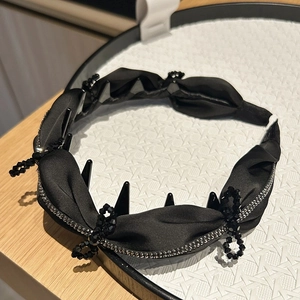 Dettaglio di cerchietto in raso nero a pieghe con decorazione di perline incrociate