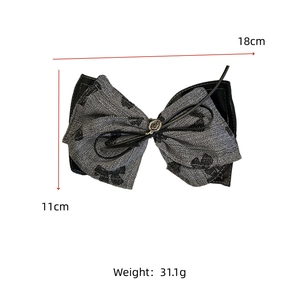 Detailed view of oversized grey tweed bow hair accessory with 18cm width and metal logo