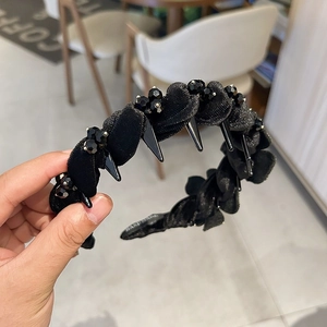Detailaufnahme von schwarzem Stoffstirnband mit Perlen und Punk-Spikes in der Hand