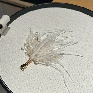 Detailed view of elegant white feather hair clip with pearls and embroidery on gold base