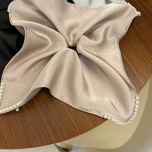 Détail d'un chouchou en satin champagne avec bordure en perles sur fond en bois