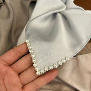 Détail d'un chouchou en satin bleu avec des perles blanches cousues sur le bord