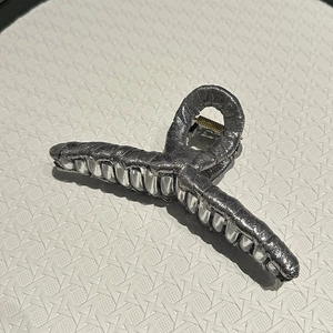 Detail of silver grey fabric wrapped hair claw clip with pleated texture and silver teeth