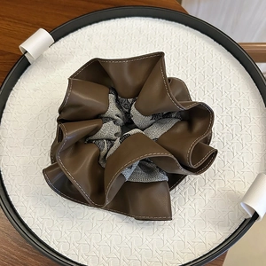 Fashionable PU leather and striped fabric scrunchie with stitching on wood surface