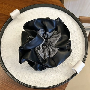 Detail of scrunchie with black faux leather and grey fabric in a minimalist tray