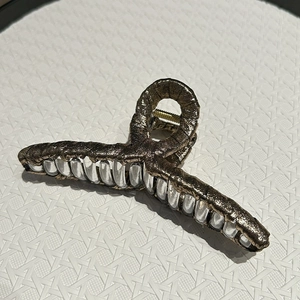Detailed macro of large bronze fabric claw clip with metallic texture and clear frame