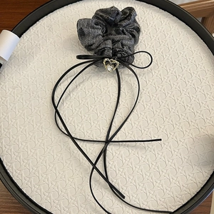 Detail of metallic black scrunchie with a black bow and gold heart charm with zircon