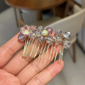 Detail of three purple crystal flowers on a golden metal hair comb held in hand