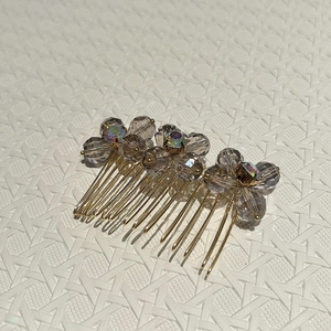 Close-up of golden metal hair comb with grey crystal flower clusters on white surface