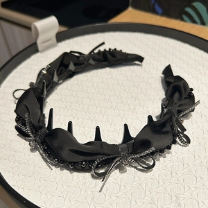Detail view of black satin headband with pleated fabric and metal chain trim