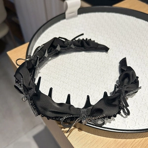 Detailed close-up of a black satin headband with bow decoration and beaded edge detail