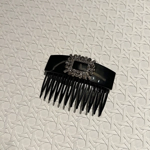 Detailed close-up of a black resin hair comb with a luxurious crystal square buckle