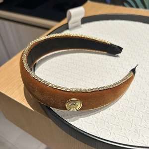 Detailed close-up of brown velvet headband with gold trim and vintage metal emblem