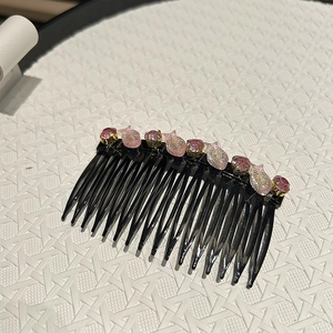 Dettaglio di perline di cristallo rosa e ciondoli a pesce su un pettine nero