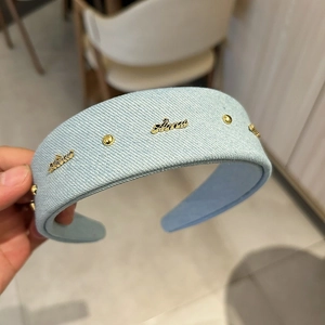 Detail of light blue denim headband with gold metal lettering and vintage rivets