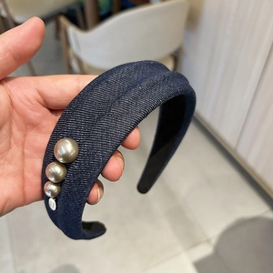 Détail d'un serre-tête en jean bleu foncé avec bord large et trois perles dorées