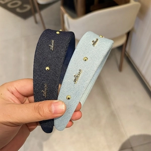 Close-up of denim headband featuring golden rivets and Aivai metallic decorative lettering