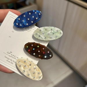 Detailed view of four colorful acetate hair clips with inlaid rhinestones on a card