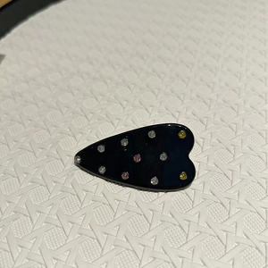 Détail d'une pince à cheveux noire en forme de cœur avec strass roses et jaunes