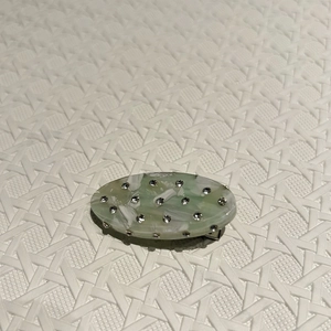 Detail of light green marble oval hair clip with sparkling rhinestones on textured fabric
