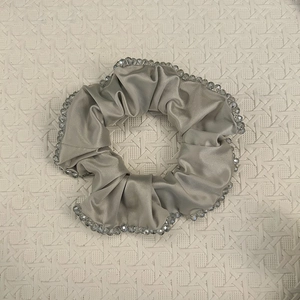 Silver satin hair scrunchie with transparent crystal beads on beige woven background
