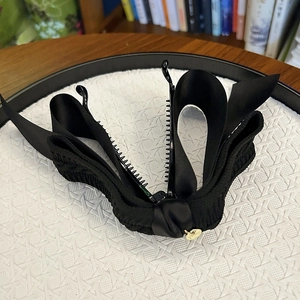 Detailed macro view of black knit bow banana clip with golden logo and plastic teeth