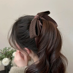 Detail of a dark brown knit and satin bow banana clip on a high ponytail for women
