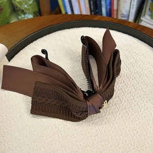 Close-up of brown knit bow banana clip with golden button and non-slip inner teeth
