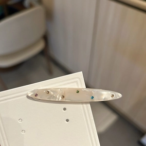 Dettaglio del fermaglio per capelli in acetato con strass colorati su cartoncino