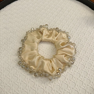 Close-up of elegant beige satin scrunchie decorated with transparent crystal beads