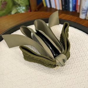 Detailed close-up of textured knit and army green satin ribbon fabric on a banana hair clip