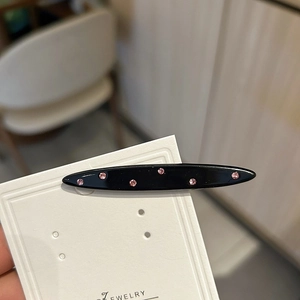 Dettaglio di un fermaglio per capelli nero in acetato con strass rosa su carta