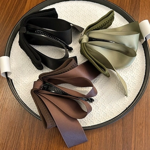 Detail of three textured knit bow banana clips in black, green, and brown in a tray
