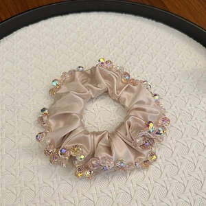 Detail of champagne satin scrunchie with faceted crystal beads on a textured tray
