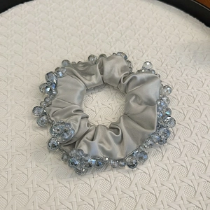 Elegant silver satin scrunchie with blue crystal beads on white texture tray