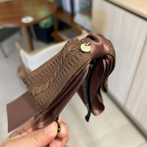 Detail of dark brown knitted bow hair clip with golden pendant and anti-slip teeth