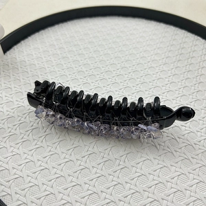 Detail of banana hair clip with purple crystal beads on glossy black teeth