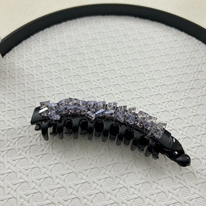 Close-up of black resin banana hair clip with purple crystal rhinestones on woven texture