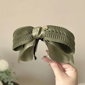 Detail of olive green knit bow banana hair clip with handmade gold metal logo plate
