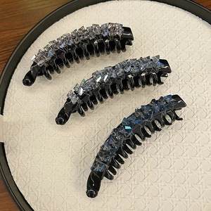 Three large banana hair clips with blue crystal beads on a textured white round plate
