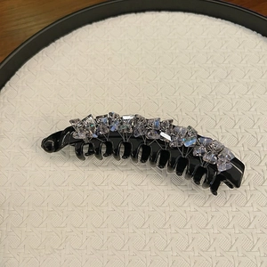 Macro shot of black banana clip with crystal rhinestones on a white textured background
