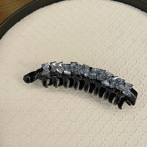 Detailed close-up of large banana hair clip with light blue and clear crystals on black resin
