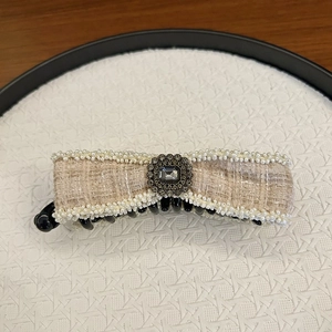 Detail of tweed bow hair clip with faux gemstone and pearl beads on a neutral tray