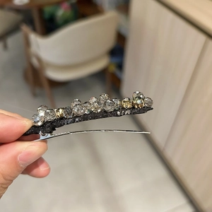 Dettaglio ravvicinato di un fermaglio per capelli con cristalli grigi e perline dorate