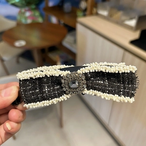Close-up of a tweed bow hair clip with white pearl edges and a crystal centerpiece