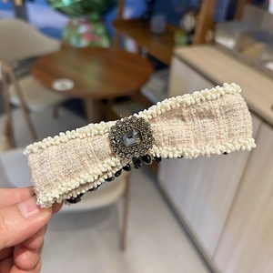 Close-up of cream tweed bow hair clip with pearl edges and center rhinestone detail