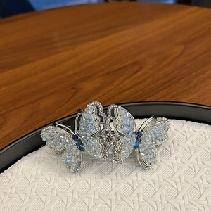 Exquisite silver butterfly hair clip with blue crystals on a white woven tray detail