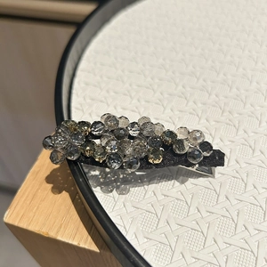 Dettaglio macro del fermaglio in cristallo con perle grigio fumo sfaccettate su base nera chic