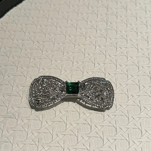 Détail d'une pince à cheveux nœud argentée avec strass et pierre centrale vert émeraude